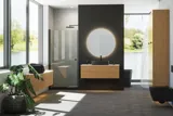 Minimalist and sleek bathroom inspiration with vanity unit, base cabinets, and tall cabinets in golden oak, large round mirror with light control, colored toilet, and countertop sink