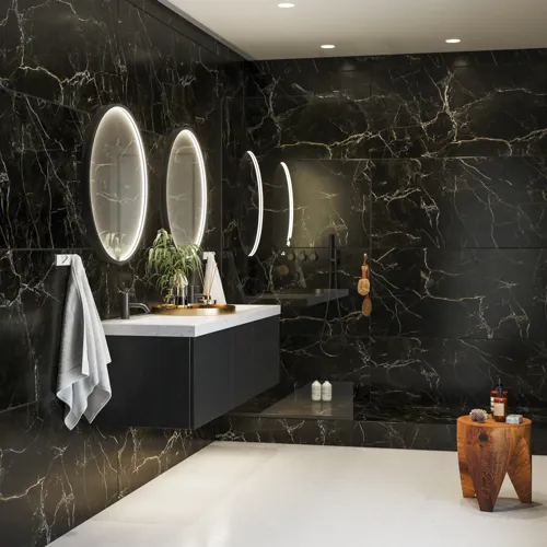 Elegant and modern bathroom inspiration with dark marble walls, round illuminated mirrors with black frames, wall-mounted vanity unit with double sinks, and a spacious shower area