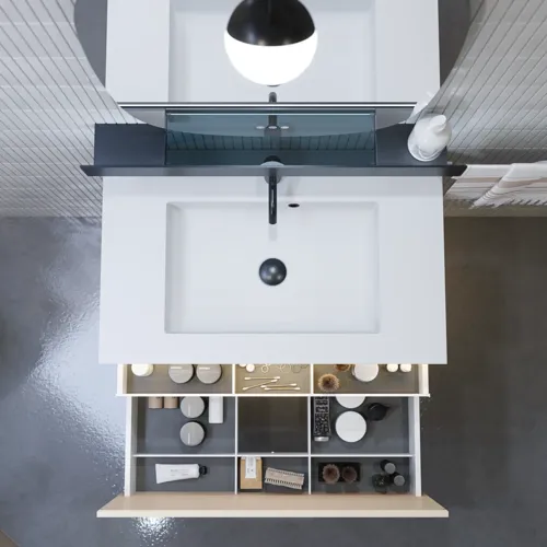 Stylish bathroom inspiration with beige vanity unit with inner drawer, upper cabinet, open shelf, oval mirror with lighting, matching pendants, shelf under the mirror, and wall-mounted toilet. Walls with light, elongated tiles.