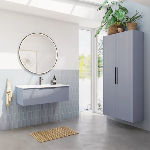 Bathroom inspiration with elongated light blue tiles and concrete floor, elegant light blue vanity unit with beautiful narrow stripes, sleek and thin sink, double tall cabinet with narrow stripes, and a minimalist round mirror with a black edge and light.